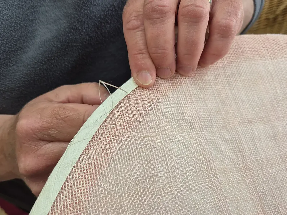 Susan sewing trim on a hat brim.