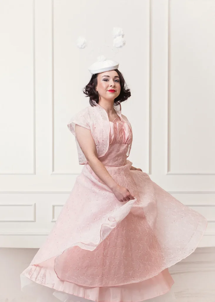 Bride wearing a pink wedding dress and a white bridal headpiece with three pompoms.