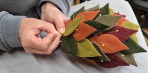 Close-up of Susan sewing some felt leaves for a hat decoration.